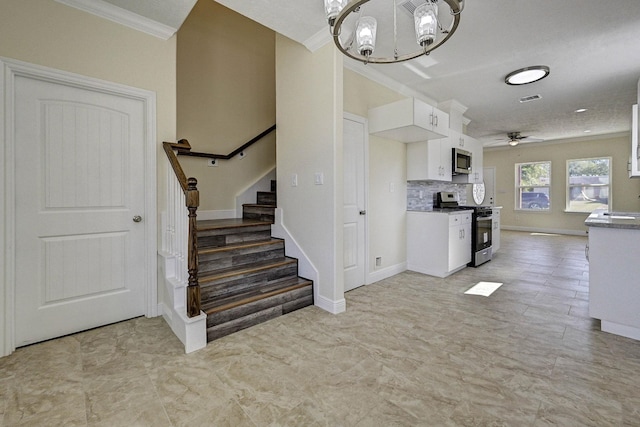 kitchen with white cabinetry, stainless steel appliances, decorative light fixtures, ceiling fan with notable chandelier, and ornamental molding