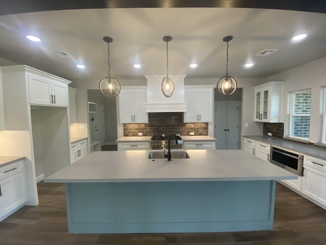 kitchen with a kitchen island with sink, white cabinets, and hanging light fixtures