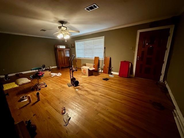 interior space featuring visible vents, ornamental molding, a ceiling fan, wood finished floors, and baseboards