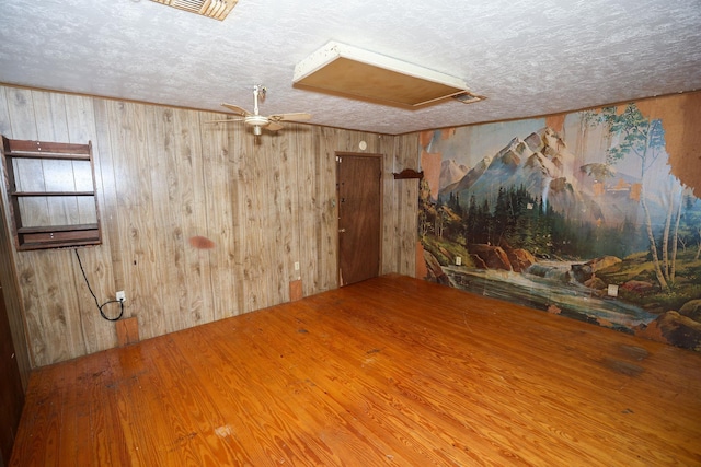 empty room with hardwood / wood-style flooring, ceiling fan, wooden walls, and a textured ceiling