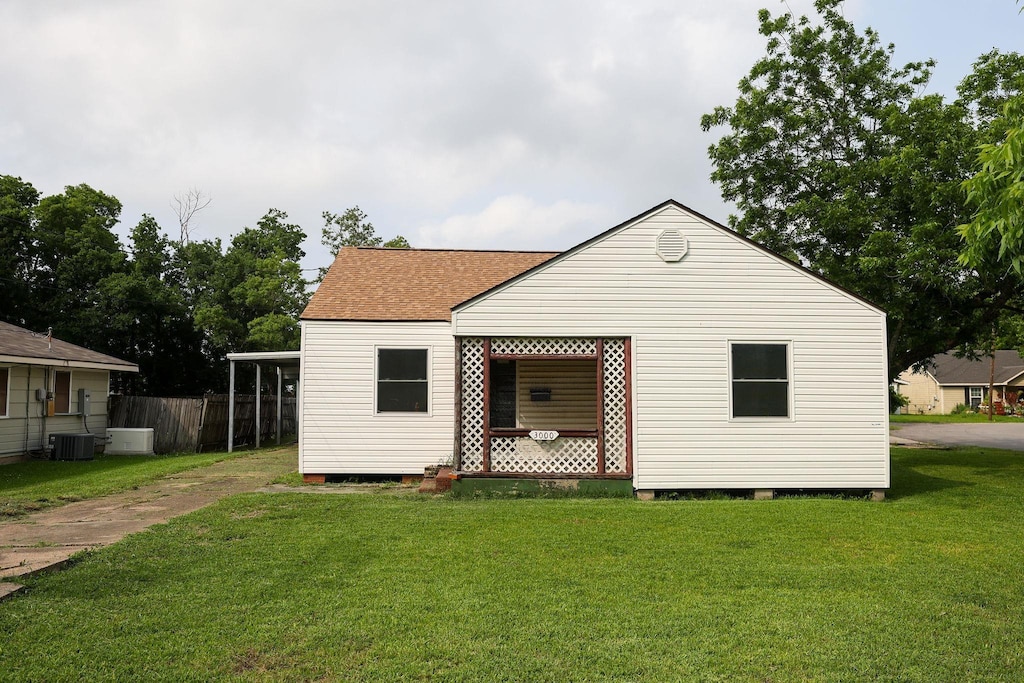 rear view of property featuring central AC unit and a lawn