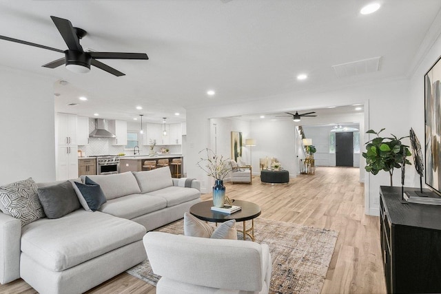 living room with ceiling fan, sink, ornamental molding, and light wood-type flooring