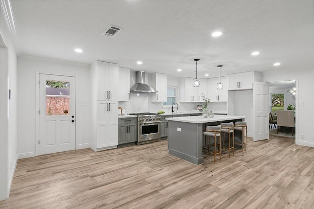 kitchen with wall chimney exhaust hood, stainless steel range, pendant lighting, white cabinets, and a center island