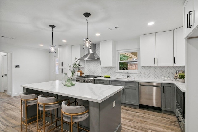 kitchen featuring dishwasher, a center island, white cabinets, wall chimney range hood, and hanging light fixtures