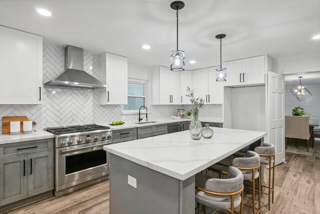 kitchen featuring sink, high end stainless steel range, wall chimney exhaust hood, decorative light fixtures, and white cabinetry