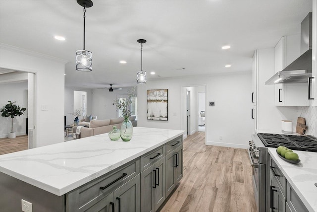 kitchen featuring backsplash, white cabinets, hanging light fixtures, stainless steel stove, and wall chimney exhaust hood