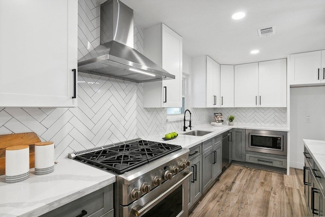 kitchen with white cabinets, wall chimney range hood, sink, and appliances with stainless steel finishes