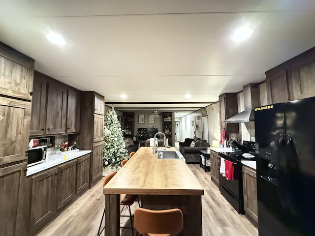 kitchen featuring black appliances, a sink, open floor plan, wall chimney range hood, and dark brown cabinets