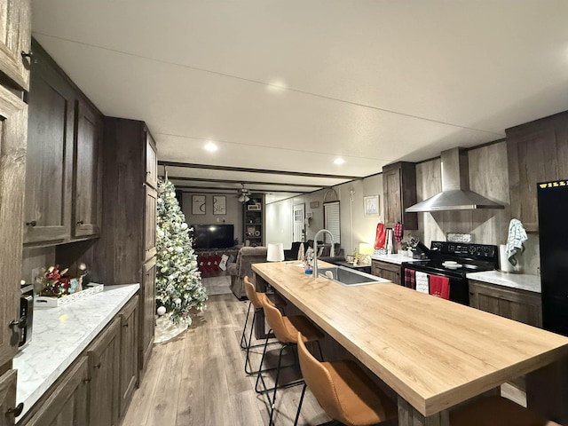 kitchen with black appliances, light wood-style flooring, a sink, open floor plan, and wall chimney exhaust hood