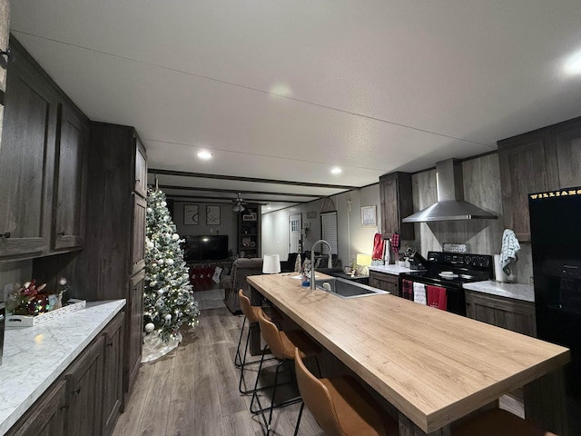 kitchen with wood finished floors, a sink, black appliances, wall chimney range hood, and open floor plan