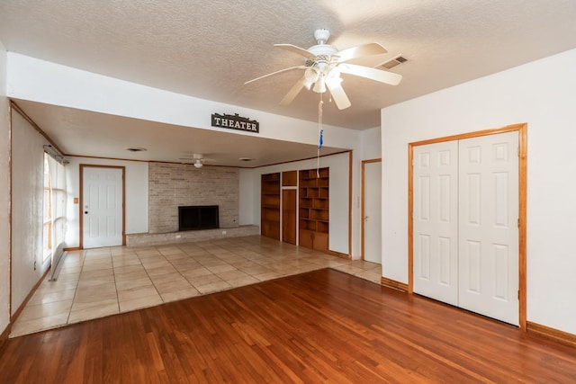 unfurnished living room featuring ceiling fan, a fireplace, light hardwood / wood-style floors, and a textured ceiling