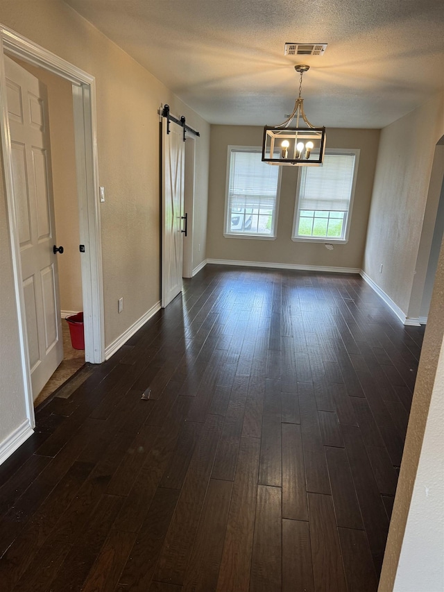 unfurnished dining area with a barn door, dark hardwood / wood-style flooring, and a chandelier