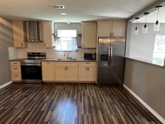 kitchen featuring light stone countertops, sink, wall chimney range hood, pendant lighting, and appliances with stainless steel finishes