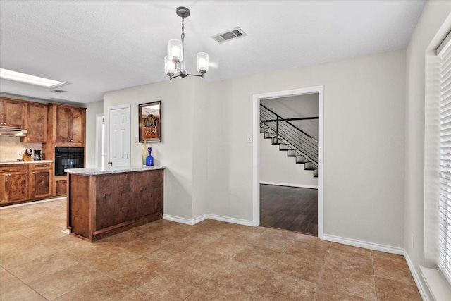 kitchen featuring pendant lighting, decorative backsplash, black oven, a notable chandelier, and kitchen peninsula