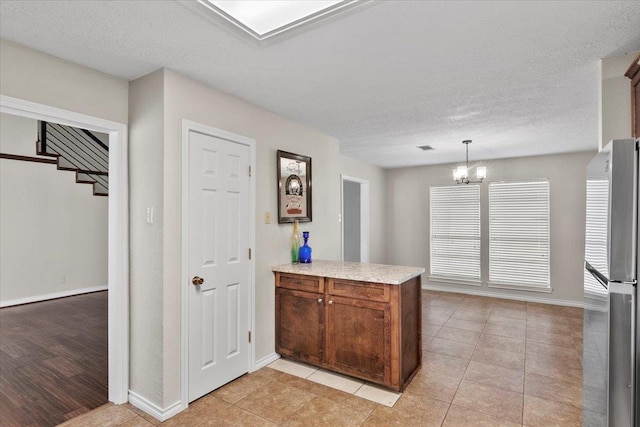 kitchen with kitchen peninsula, stainless steel fridge, pendant lighting, an inviting chandelier, and light tile patterned flooring