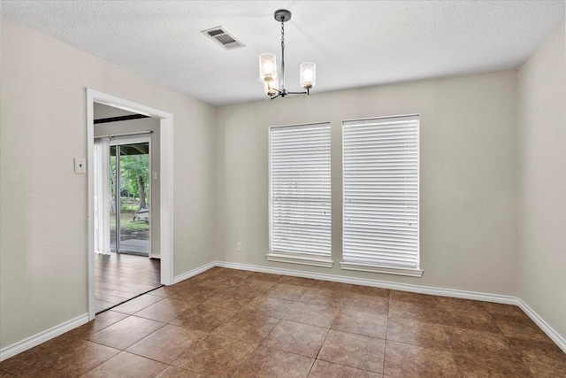 tiled spare room with a textured ceiling and an inviting chandelier