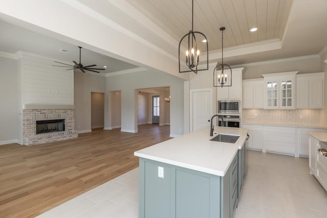 kitchen featuring appliances with stainless steel finishes, decorative light fixtures, white cabinetry, a tray ceiling, and a center island with sink