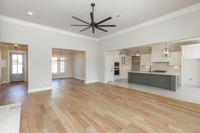 unfurnished living room featuring crown molding, sink, ceiling fan with notable chandelier, and light wood-type flooring