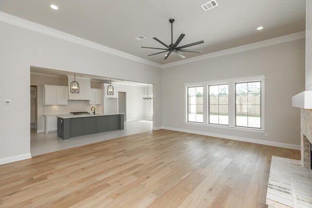 unfurnished living room featuring a brick fireplace, crown molding, and light hardwood / wood-style floors