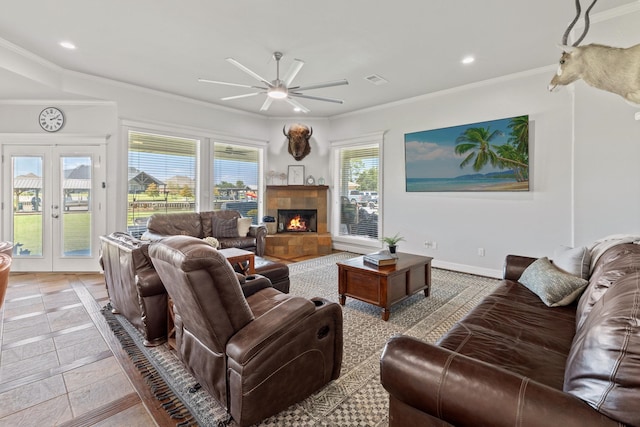 living room with french doors, ornamental molding, ceiling fan, light tile patterned floors, and a tiled fireplace