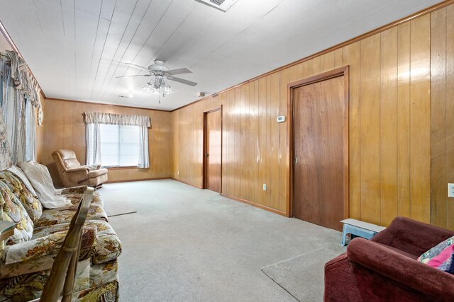 living area featuring light colored carpet, ceiling fan, and wooden walls