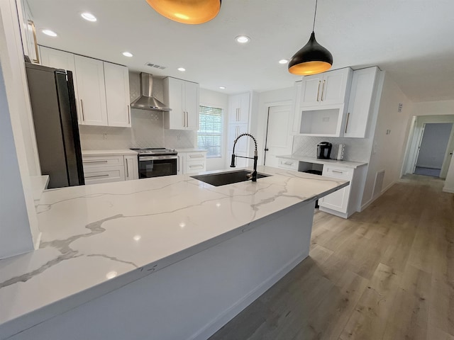 kitchen with light stone counters, wall chimney exhaust hood, stainless steel appliances, sink, and white cabinetry