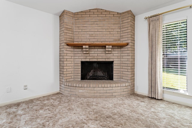 unfurnished living room with carpet flooring, vaulted ceiling, a brick fireplace, and baseboards