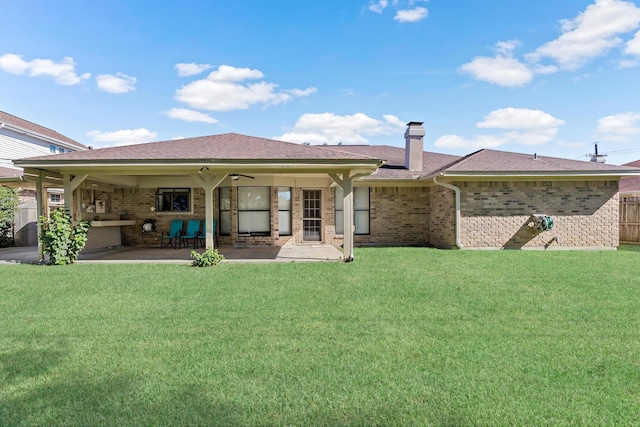 back of house with a lawn, a chimney, brick siding, and a patio