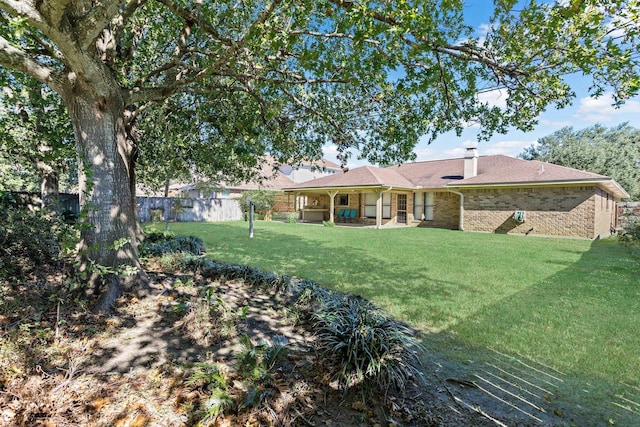 back of house featuring a chimney, fence, a yard, and brick siding