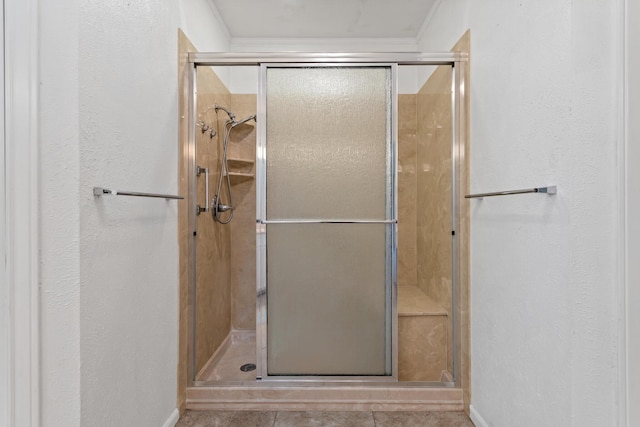 bathroom featuring a textured wall, baseboards, tile patterned floors, and a stall shower