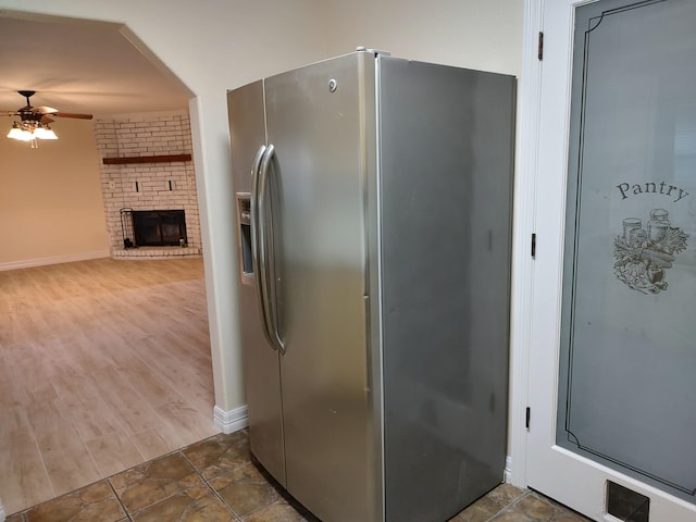 kitchen featuring dark hardwood / wood-style floors, stainless steel fridge, ceiling fan, and a fireplace