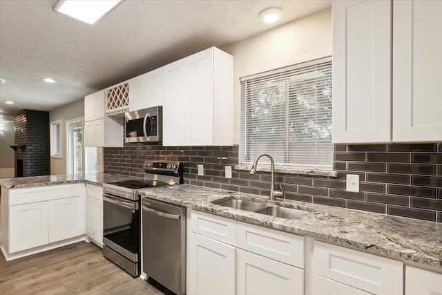 kitchen with sink, stainless steel appliances, a textured ceiling, white cabinets, and light wood-type flooring