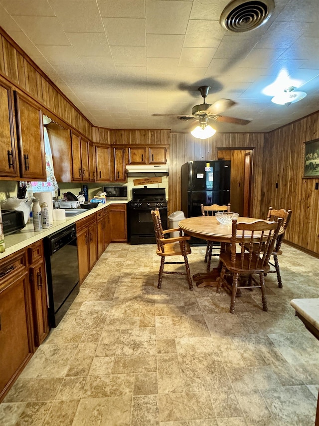 3704 Nightingale St, Orange, TX 77630 - kitchen with black appliances, under cabinet range hood, light countertops, wood walls, and brown cabinets