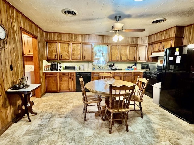 3704 Nightingale St, Orange, TX 77630 - kitchen featuring black appliances, wood walls, brown cabinetry, under cabinet range hood, and washer / dryer