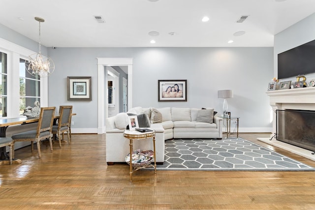 living room featuring a notable chandelier, recessed lighting, visible vents, a fireplace with raised hearth, and wood finished floors