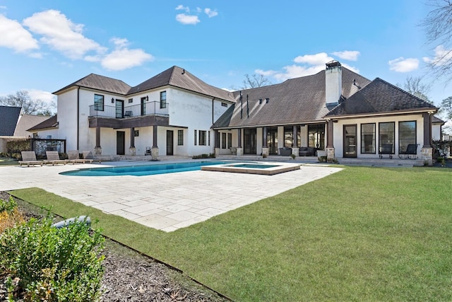 back of property with a balcony, a pool with connected hot tub, a yard, a chimney, and a patio area