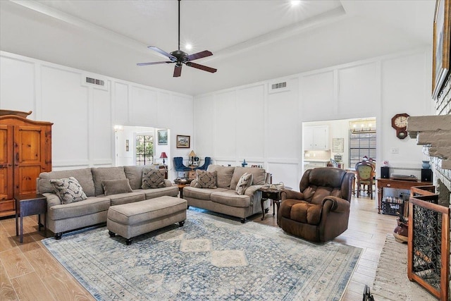 living room featuring ceiling fan with notable chandelier, a high ceiling, a tray ceiling, and light hardwood / wood-style flooring