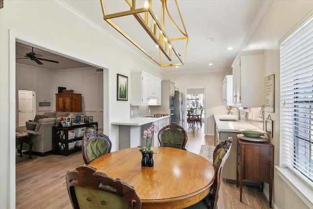 dining space with ceiling fan with notable chandelier, sink, ornamental molding, and light wood-type flooring