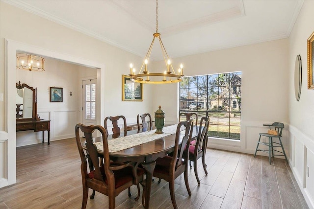 dining area with a notable chandelier, a raised ceiling, hardwood / wood-style floors, and ornamental molding