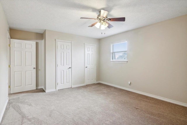 unfurnished bedroom with a textured ceiling, ceiling fan, light carpet, and multiple closets