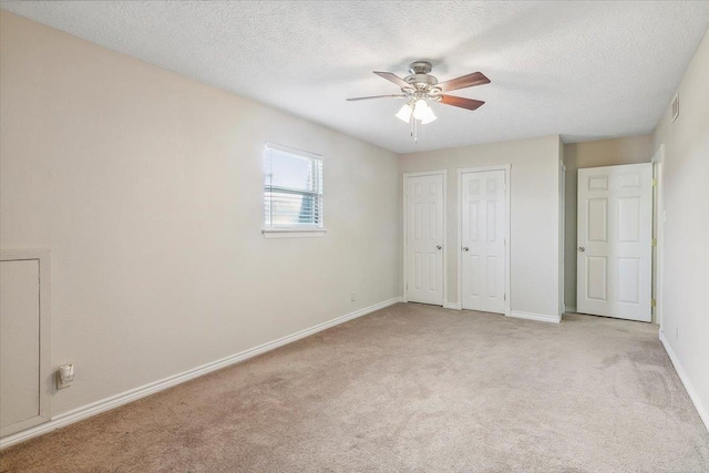 unfurnished bedroom with ceiling fan, light colored carpet, a textured ceiling, and two closets