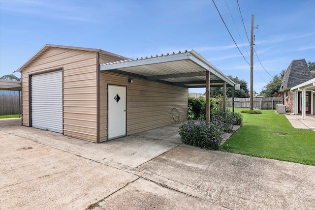 view of outdoor structure featuring a lawn, cooling unit, a carport, and a garage