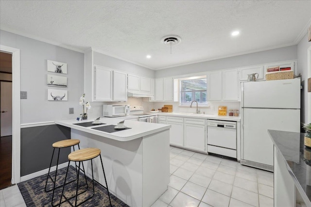 kitchen featuring white appliances, under cabinet range hood, a sink, a peninsula, and white cabinetry