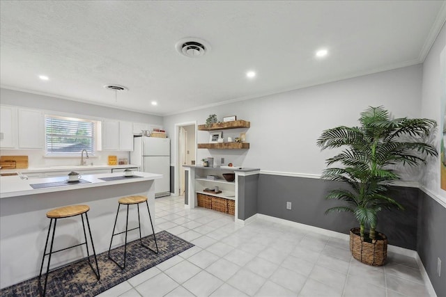 kitchen featuring freestanding refrigerator, open shelves, a breakfast bar area, light countertops, and white cabinets