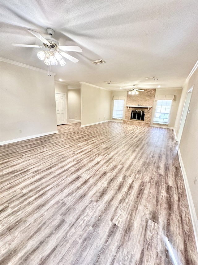 unfurnished living room featuring ceiling fan, light hardwood / wood-style flooring, a textured ceiling, a fireplace, and ornamental molding