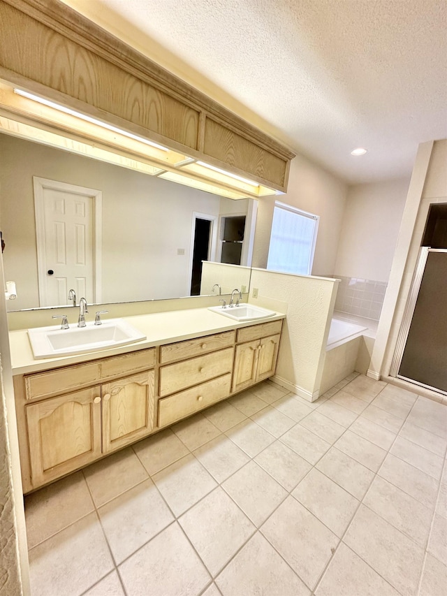 bathroom with tile patterned flooring, a textured ceiling, vanity, and tiled tub