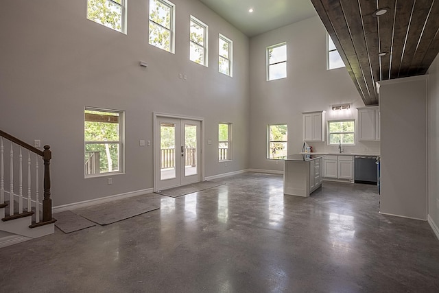 unfurnished living room featuring a sink, baseboards, finished concrete flooring, french doors, and stairway