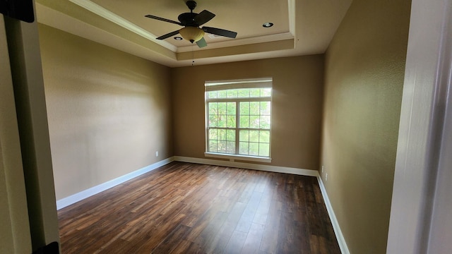 spare room featuring ceiling fan, a raised ceiling, dark wood finished floors, baseboards, and ornamental molding