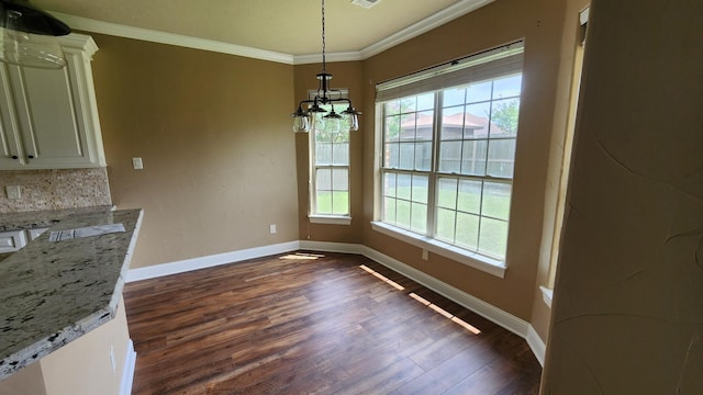 unfurnished dining area featuring dark wood-type flooring, baseboards, a notable chandelier, and crown molding