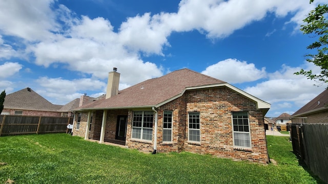 back of house featuring a chimney, a fenced backyard, a yard, roof with shingles, and brick siding